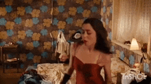 a woman in a red dress is standing on a bed in a room with a floral wallpaper .