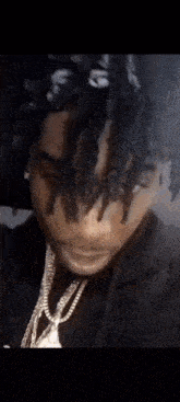 a close up of a man with dreadlocks and a necklace .