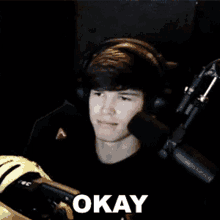 a young man wearing headphones is sitting in front of a microphone with the word okay written on his face .