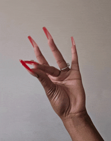 a woman 's hand with long red nails and a silver ring on her finger