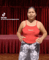 a woman in a red tank top and floral pants is standing on a stage .