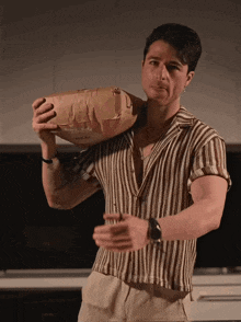 a man wearing a striped shirt is holding a bag that says ' bread ' on it