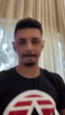 a man with a beard is wearing a black t-shirt with a red and white triangle on it .