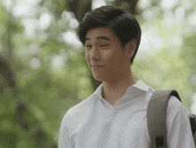 a man wearing a white shirt and carrying a backpack makes a funny face