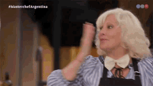 a woman in a striped shirt and apron is dancing in front of a masterchef argentina logo