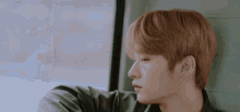a young man with red hair is sitting in front of a window and looking out .