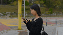 a woman in a black sweater looks at her cell phone
