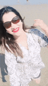 a woman wearing sunglasses and red lipstick is smiling on the beach