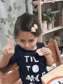 a little girl wearing a shirt that says til to nope is eating a snack
