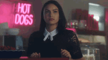 a woman is sitting at a counter in front of a hot dogs sign .