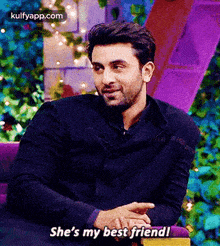 a man in a black jacket is sitting in a purple chair and says she 's my best friend .