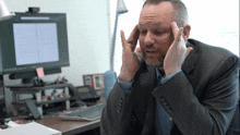 a man in a suit holds his head while talking on a phone