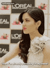 a woman in a white dress is standing in front of a wall with a flower on her shoulder .