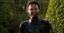 a man covered in black paint is smiling in front of trees