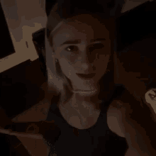 a woman in a black tank top is smiling in a dark room