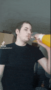 a man in a black shirt is drinking a bottle of orange juice from a glass