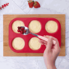 a person is using a spoon to add berries to a muffin pan