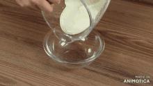 a person pouring a white liquid into a glass bowl with the words made in animatica on the bottom