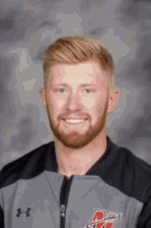 a man with a beard is wearing an under armour jacket and smiling for the camera