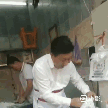 a man in a white shirt is standing next to another man in an apron in a kitchen