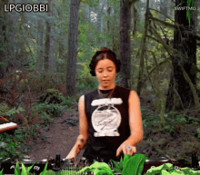 a woman in a black tank top is playing a dj set in the woods with the words lpgiobbi above her