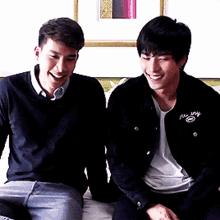 two men are sitting next to each other on a bed and one of them is wearing a black jacket that says always