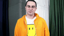 a man wearing glasses and an orange hoodie with a yellow smiley face on his shirt