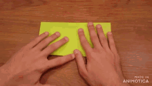 a person is folding a piece of yellow paper on a wooden table