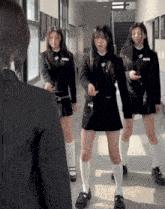 a woman in a black suit stands in a hallway with three girls in school uniforms
