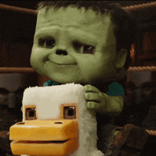 a green monster is holding a stuffed duck with a yellow beak