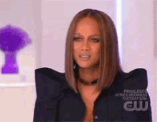 a woman wearing a black jacket with a purple vase in the background