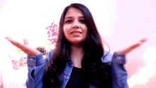 a young woman in a denim jacket is standing in front of a pink wall .