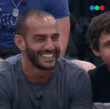 a man with a beard wearing a grey shirt is smiling with his eyes closed
