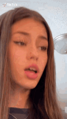 a young girl with long brown hair is making a funny face while looking at the camera .