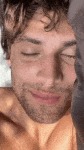 a man without a shirt is laying in bed with his eyes closed .