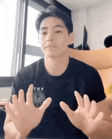 a young man in a black shirt is sitting at a table with his hands outstretched .