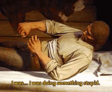 a painting of a man laying on a bed with the words " i was doing something stupid " above him