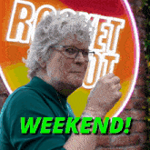 an older woman stands in front of a sign that says rocket out weekend