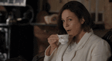 a woman sitting in a chair drinking from a white cup