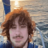 a man with curly hair and a beard is sitting on a boat in the water .