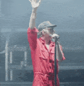 a man in a red jumpsuit singing into a microphone with his hand in the air