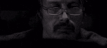 a man wearing glasses and a beard is looking at something in a black and white photo .
