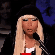 a woman with blonde hair is talking into a microphone while wearing a black hoodie .