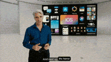 a man in a blue shirt is standing in front of a large screen that says ios on it .