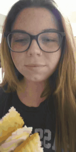 a woman wearing glasses and a black shirt with the number 22 on it is eating a sandwich