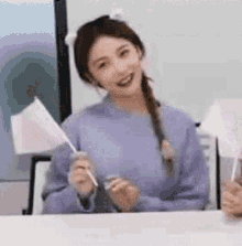 a woman in a purple sweater is sitting at a table holding a small white flag .