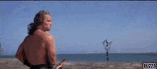 a shirtless man is holding a fishing rod with buzza written on the bottom right corner