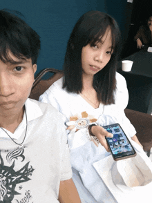 a girl sitting next to a man holding a cell phone that says samsung on it