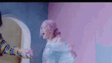 a woman with pink hair is standing next to a man in a plaid shirt in a room .