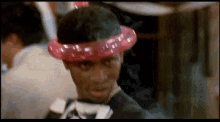 a man wearing a pink balloon hat and a tuxedo is looking at the camera .